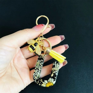 Detail of letter U keychain with real dried daisies, resin gold foil, and bee charm