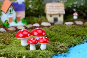 Macro di quattro funghi in miniatura rossi e bianchi in un paesaggio fatato di muschio
