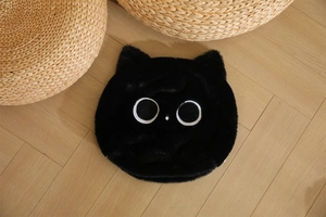 Dettaglio di un cuscino a forma di gatto nero con grandi occhi ricamati su legno