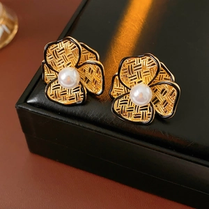 Detailed macro view of gold-plated floral earrings with pearls on black leather texture
