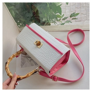 Detail of white crocodile texture handbag with bamboo handle and pink strap accents