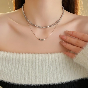 Detail view of double-layer silver necklace with bead chain and sleek snake chain on white sweater