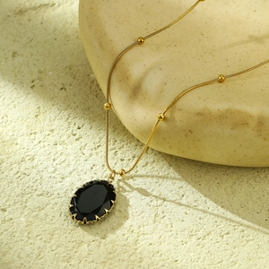 Macro detail of black oval stone pendant with gold scalloped bezel and beaded chain