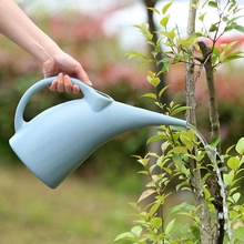 Close-up of Morandi blue plastic watering can with a long spout watering green plants