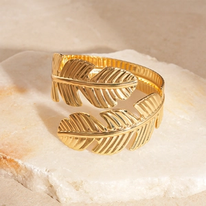 Close-up of golden leaf cuff bracelet with intricate plant texture on stone background