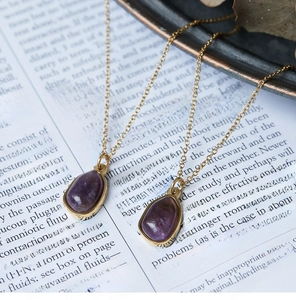 Close-up of vintage gold titanium steel necklace with oval purple gemstone on book