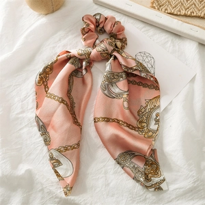 Detail of pink satin scrunchie with long ribbons and golden chain scarf print patterns