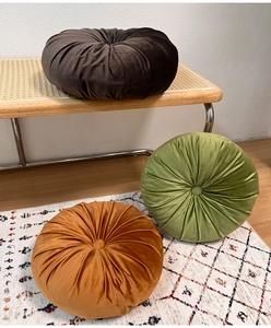 Three plush velvet pumpkin cushions in brown, olive green, and caramel on a bench