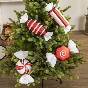 Red and white candy ornaments on Christmas tree branch with warm festive home backdrop