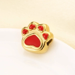 Detail view of a golden stainless steel cat paw bead with vibrant red enamel filling