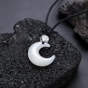 Collier croissant de lune blanc avec cordon tressé noir sur roche volcanique sombre