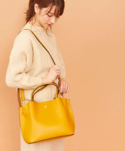 Detail of yellow lychee grain leather tote bag with metal emblem and crossbody strap