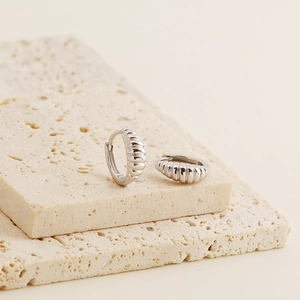 Detailed macro view of S925 sterling silver croissant earrings on beige stone stand