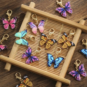 Colorful enamel butterfly charms with gold lobster clasps displayed on a bamboo stand
