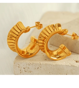 Close-up of golden teardrop earrings with 18K plated wavy texture on a natural stone base