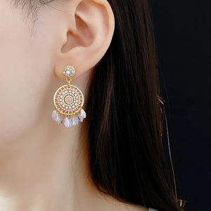 Detail of gold dreamcatcher earring with pink beads and crystal pendants on a model