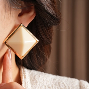 Detail of large cream white resin square stud earrings with gold metal bezel on model