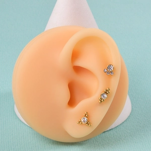 Golden plated 16G ear studs with clear zircons shown on a silicone ear model