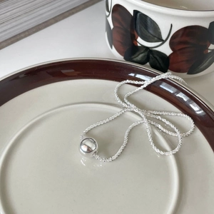 Detailed view of a minimalist silver ball pendant necklace on a ceramic jewelry tray