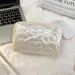 Macro detail of white quilted heart pattern cosmetic bag in glossy woven fabric