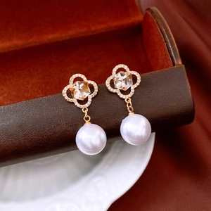 Close-up of gold clover earrings with amber stone, pavé crystals and white pearl drop