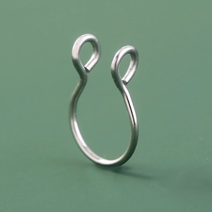 Macro detail of a silver stainless steel U-shaped nose ring on a green surface