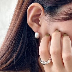 Close-up of 925 sterling silver U-shaped matte earrings and stacked rings worn by a model