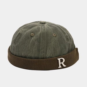 Close-up of olive green docker hat with silver metal R letter and brown ribbed cuff