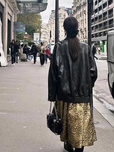 Detail of vintage black leather jacket and gold textured jacquard skirt on Paris street