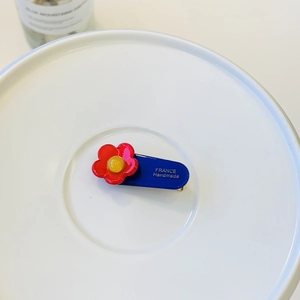 Blue and red floral handmade hair clip accessory on a white ceramic plate