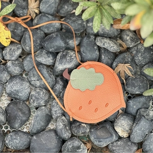 Detail view of persimmon shaped leather bag with lychee texture on natural pebbles