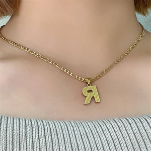 Dettaglio di una collana Figaro dorata con pendente lettera R su un maglione a coste