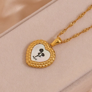 Détail d'un pendentif coeur doré avec motif floral d'avril sur fond de nacre blanche