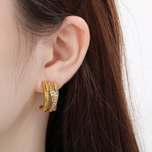 Gros plan d'une boucle d'oreille en C torsadée dorée avec strass portée par un modèle