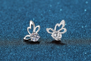 Macro shot of silver butterfly earrings with round moissanite on a dark blue glitter background