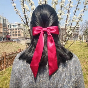 Large red satin bow hair clip with long ribbons worn by a woman outdoors