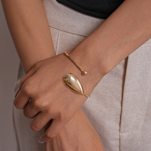 Close-up of a gold teardrop open cuff bracelet with a polished mirror finish on a wrist