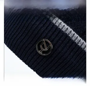 Dettaglio del berretto in maglia blu scuro con trama a coste, striscia grigia e logo in metallo