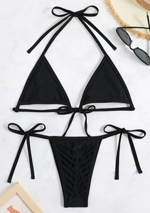 Flat lay of black lace-up bikini set on marble background with sunglasses and hat