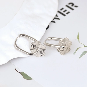 Close-up of silver oval hoop earrings with textured flower charms on a white surface