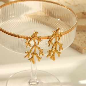 Détail de boucles d'oreilles corail doré avec texture granuleuse sur bord en verre