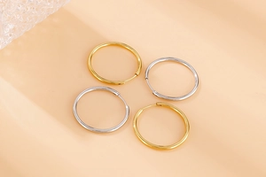 Polished gold and silver 304 stainless steel hoop earrings on an apricot surface