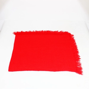 Dettaglio della sciarpa in maglia rossa con trama morbida e nappe fitte sul bordo