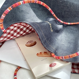 Close-up of blue denim tote bag with red checkered lining and colorful woven rope handles