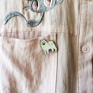 Vue détaillée d'une broche chien en émail blanc sur la poche d'une chemise rose