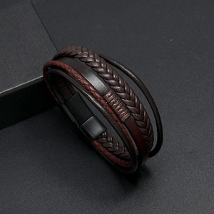 Detail of dark brown braided leather bracelet with black magnetic clasp on textured surface