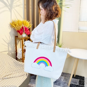 Large white canvas tote bag with embroidered rainbow and cloud patterns and tassel trim