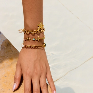Gold starfish bracelet set with pearls and shells displayed on a wrist by a pool