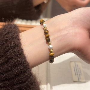 Macro view of vintage tiger eye and pearl beaded bracelet worn on a female wrist