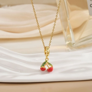 Macro shot of gold cherry pendant necklace with red crystals and green leaves